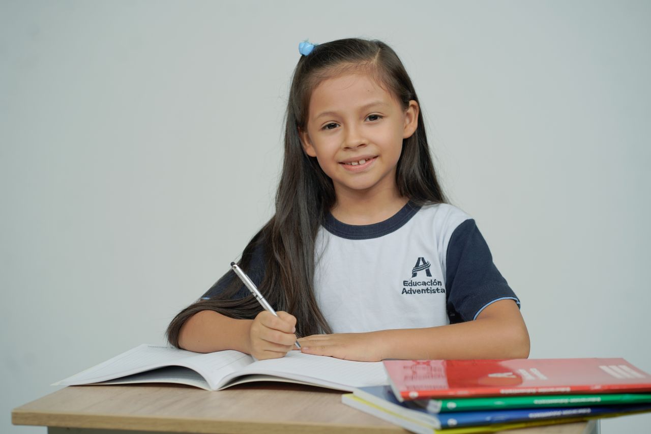 A young girl sitting at a desk, studying with open books and smiling.
